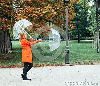 Caucasian girl in red gabardine plays with two transparent umbrellas in a park Stock Photo