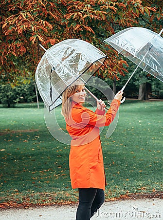 Caucasian girl in red gabardine plays with two transparent umbrellas in a park Stock Photo