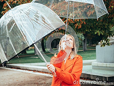 Caucasian girl in red gabardine plays with two transparent umbrellas in a park Stock Photo