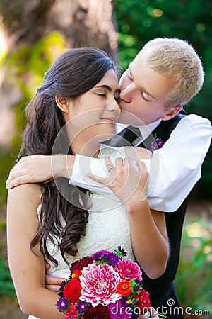 Caucasian groom lovingly kissing his biracial bride on cheek. Di Stock Photo