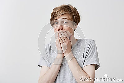 Caucasian guy with bugged blue eyes, covers mouth in terror, being emotional or scared after hearing shocking news on Stock Photo