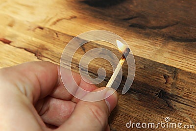 A Caucasian hand holding a lit match. This image also contains a wooden background and can be used to represent fire starting or a Stock Photo