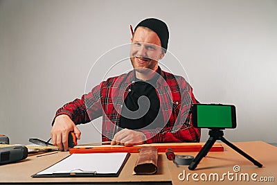 A Caucasian male builder blogger in uniform talks on a smartphone. The concept of a carpenter`s video blog in the workshop Stock Photo