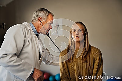 Caucasian male Doctor diagnosing female patients illness in consultation room, stethoscope lung test, deep breathing Stock Photo