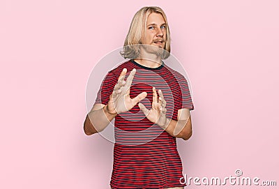 Caucasian man with blond long hair wearing casual striped t shirt disgusted expression, displeased and fearful doing disgust face Stock Photo