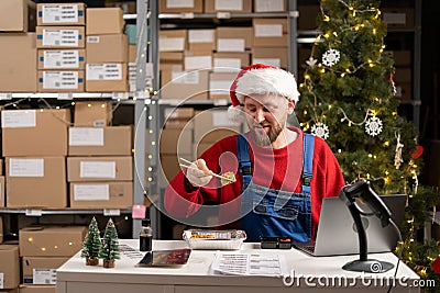 Caucasian man eating sushi rolls with chopsticks sitting at working desk with laptop at warehouse. Hungry male eating Stock Photo