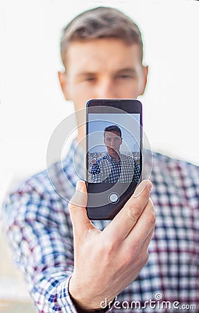 Caucasian men is making a selfie portrait with the help of smart phone. There is a city on the back ground. Dressed into Stock Photo