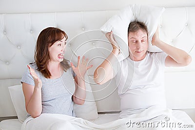 Caucasian middle age family couple angry shouting in bed. Conflict relationship concept. Husband cover ears by hands and wife Stock Photo