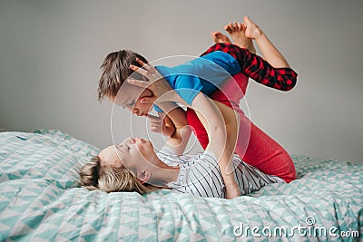Caucasian mother and boy son playing in bedroom at home. Mom rocking child on her knees feet legs. Family having fun together. Stock Photo