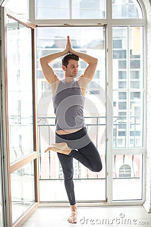 Sporty man practicing yoga in white room with big window. tree pose Stock Photo