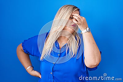 Caucasian plus size woman standing over blue background tired rubbing nose and eyes feeling fatigue and headache Stock Photo