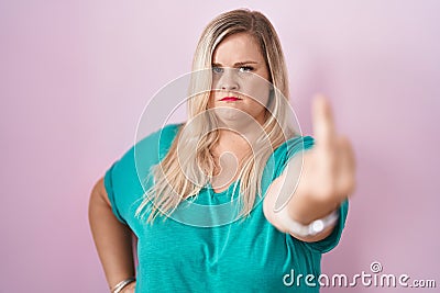 Caucasian plus size woman standing over pink background showing middle finger, impolite and rude fuck off expression Stock Photo