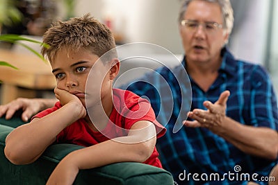 Caucasian sad boy with hand on chin looking away while sitting with grandfather on sofa Stock Photo