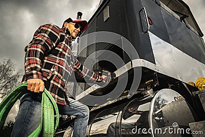 Semi Truck Driver Preparing Trailer Cargo Straps Next to His Tractor Stock Photo