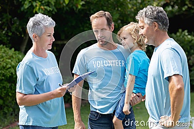 Caucasian senior couple with clipboard and father carrying son in volunteer shirts talking in field Stock Photo