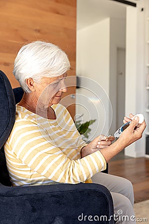 Caucasian senior woman measuring her blood sugar using glucometer at home Stock Photo