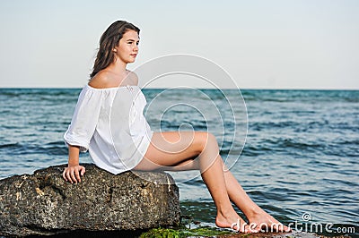 Caucasian teen girl in bikini and white shirt lounging on lava rocks by the ocean Stock Photo