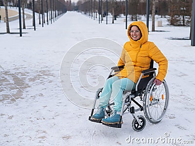 Caucasian woman with disabilities rides on a chair in the park in winter. Girl on a walk in a wheelchair. Stock Photo