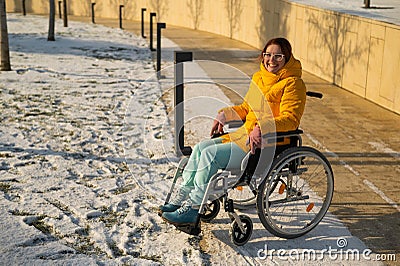 Caucasian woman with disabilities rides on a chair in the park in winter. Girl on a walk in a wheelchair. Stock Photo