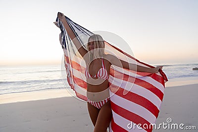 Caucasian woman holding and waving an US flag at the beach. Stock Photo