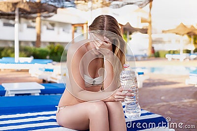 Caucasian woman got heatstroke or hangover seating on the beach with a bottle of water. sunstroke, illness while summer traveling Stock Photo