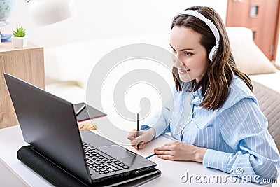 Caucasian woman with headphones writes in notebook, looks at laptop screen, remote work at home, home training Stock Photo