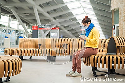 Caucasian woman in mask uses mobile on a bench in a public place. Stock Photo