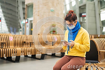 Caucasian woman in mask uses mobile on a bench in a public place. Stock Photo