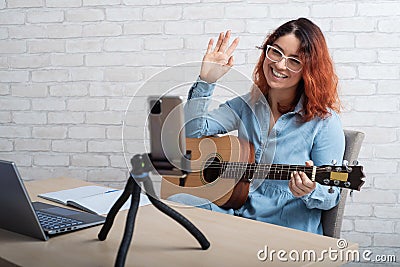 Caucasian woman playing guitar live on a smartphone. The girl leads a music video blog Stock Photo