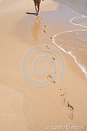 Caucasian woman seen from her back walking on an empty beach. Footprints in the sand. Circulatory system is improved by aerobic ex Stock Photo