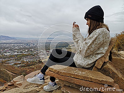 Caucasian woman sitting on a rocky sofa taking a photo to the view from Living Room Trailhead hike Stock Photo