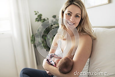 Woman in her bedroom on the white cushions, smiling and breastfeed her baby. Stock Photo