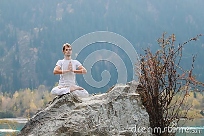 Caucasian yoga man in outdoor meditation sitting on lonely rock island of mountain lake Stock Photo