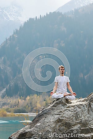 Caucasian yoga man in outdoor meditation sitting on lonely rock island of mountain lake Stock Photo