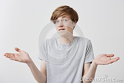 Caucasian young male with fair hair and blue eyes has hesitant and displeased expression, gestures doubtfully, being Stock Photo