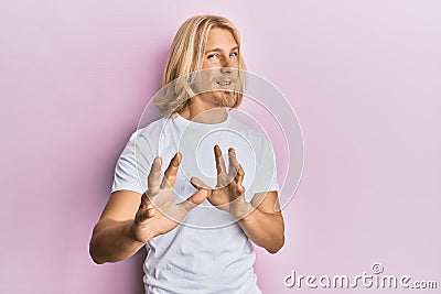 Caucasian young man with long hair wearing casual white t shirt disgusted expression, displeased and fearful doing disgust face Stock Photo