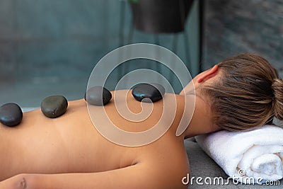 Caucasian young woman receiving hot stone massage lying on the massage table Stock Photo