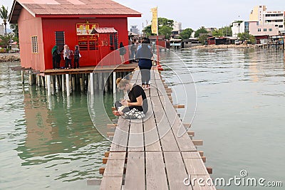 Caucasian young woman using her smartphone on narrow wooden pier Editorial Stock Photo
