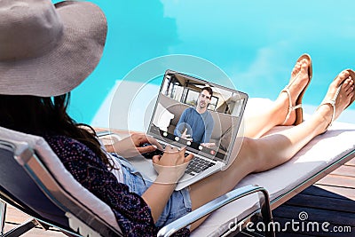 Caucasian young woman video calling male coworker through laptop on poolside during vacation Stock Photo