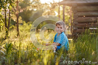Caucasoid short-haired five-year-old boy sitting in the tall grass in the garden in the summer Stock Photo