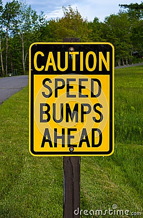 Caution speed bumps ahead sign next to a park road with lawn and trees in the background Stock Photo