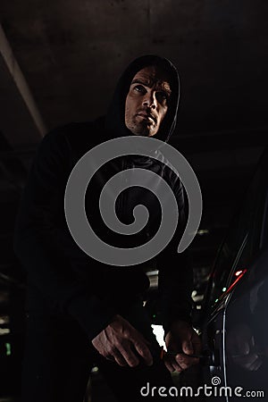 cautious male robber in black hoodie intruding car Stock Photo