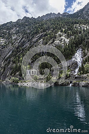 Cavallers reservoir between high mountains, a waterfall and a building of the hydroelectric power station, river Noguera de Tor in Stock Photo