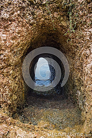 Cave with entrance to the sea. Natural tunnel in cave. Passage in rocks. Natural staircase in ocean cave. Stock Photo