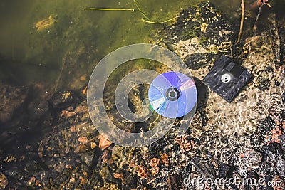 CD disk and floppy diskette are lying in the lake outdoors. Forgotten past concept in the water Stock Photo