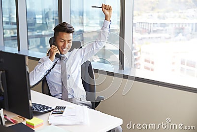 Celebrating Businessman Making Phone Call At Desk In Office Stock Photo