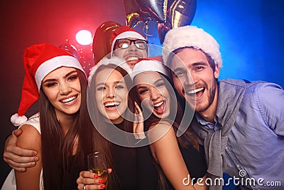 Celebrating New Year together. Group of beautiful young people in Santa hats throwing colorful confetti, looking happy Stock Photo