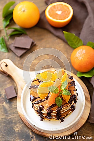 Celebrating Pancake day, healthy american breakfast. Delicious bananas pancakes with chocolate and red oranges on rustic table Stock Photo