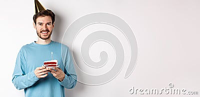 Celebration and holidays concept. Happy young man in party hat celebrating birthday, holding bday cake and smiling Stock Photo