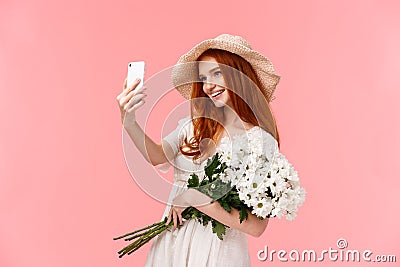 Celebration, social media and internet concept. Alluring sassy redhead female in straw hat, spring dress, holding Stock Photo
